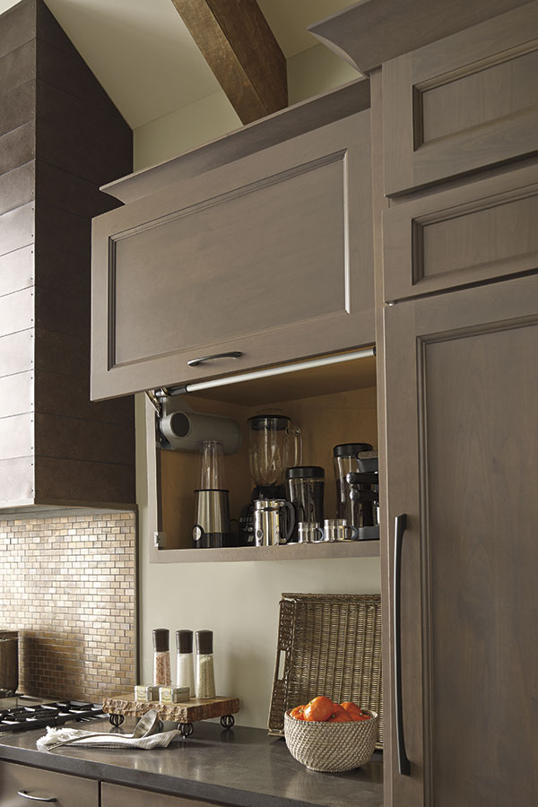 neutral colored vertical lift door hinge with kitchenware inside and bowl of fruit visible on counter